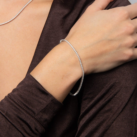 A wrist wearing a silver tennis bracelet against a dark sleeve