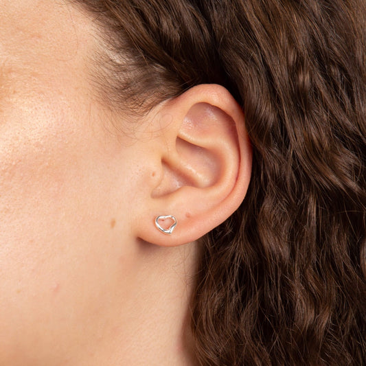 A woman wearing the Beginnings small open heart stud earrings.