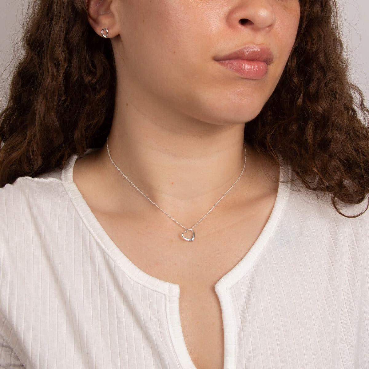 A woman wearing the Beginnings small open heart stud earrings with matching pieces.