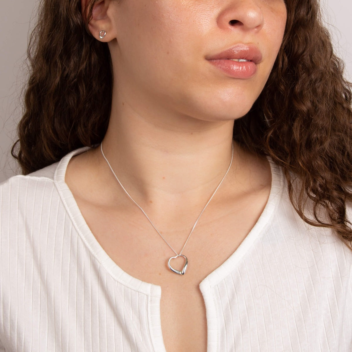 A woman wearing the Beginnings small open heart stud earrings with matching pieces.