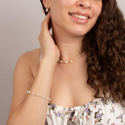 A woman wearing the Beginnings pearl bracelet with matching pearl earrings and necklace.