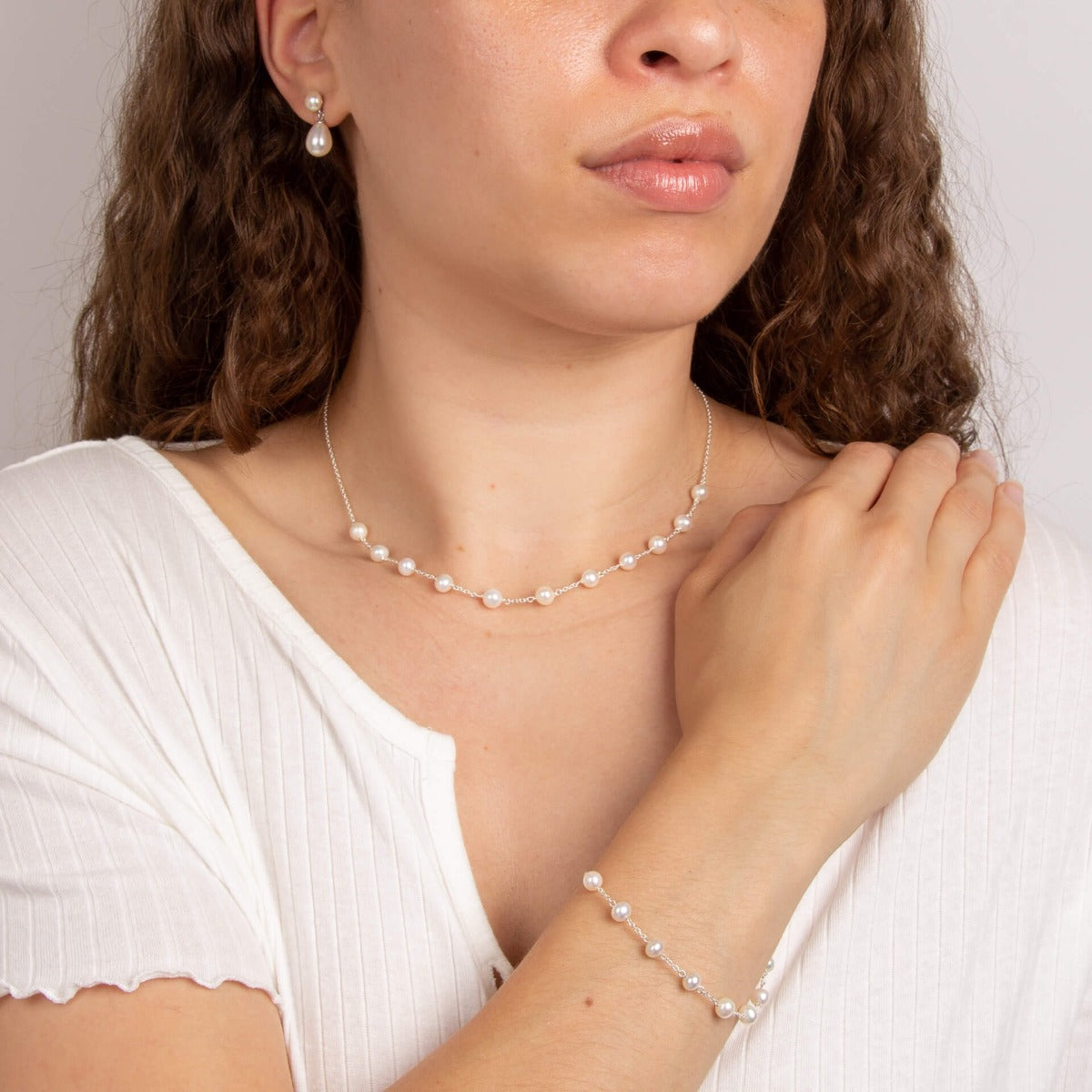 A woman wearing the Beginnings pearl bracelet with matching pearl earrings and necklace.